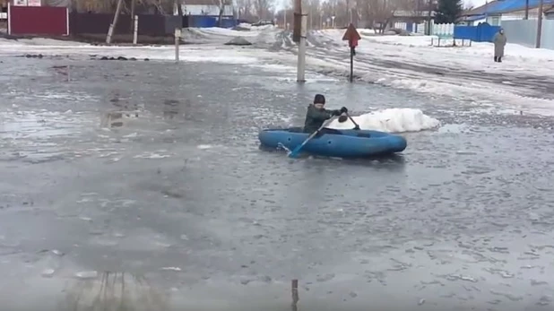 Мальчик катается на лодке по луже в бийском поселке.