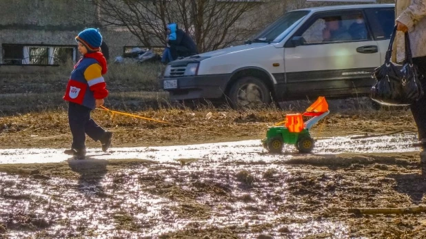 Мальчик с игрушкой шагает по луже и грязи.