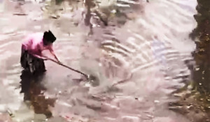 Женщина со шваброй очищает ливневку от грязи.