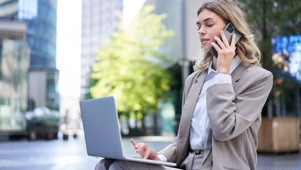 Девушка разговаривает по телефону и работает за ноутбуком.