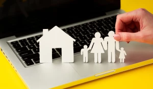 Ноутбук, бумажные фигурки домика и семьи.