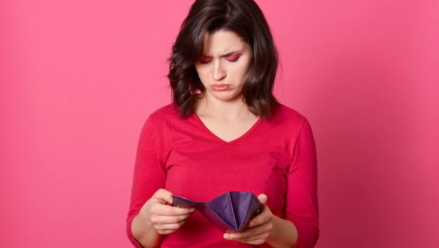 Женщина с грустью смотрит в кошелек.