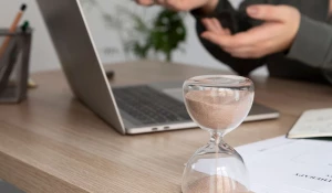 Женщина работает за ноутбуком, рядом стоят песочные часы.