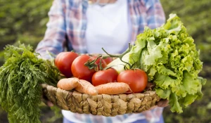 Женщина держит корзину с овощами.