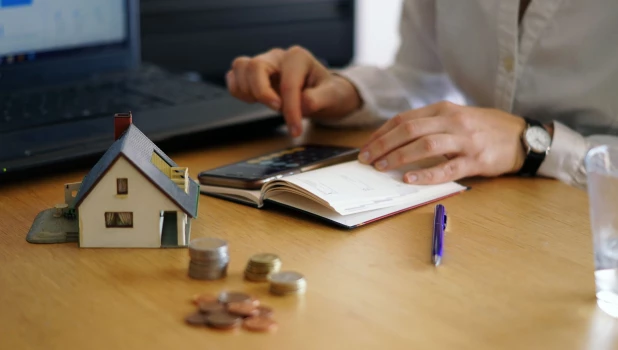 Монеты. Макет дома. Человек считает на калькуляторе.