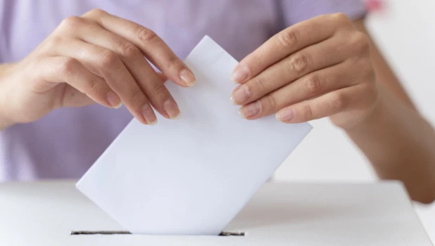 Женщина опускает бюллетень в урну для голосования.