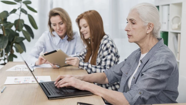 Пожилая женщина работает в офисе за ноутбуком.