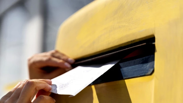 Женщина опускает письмо в почтовый ящик.